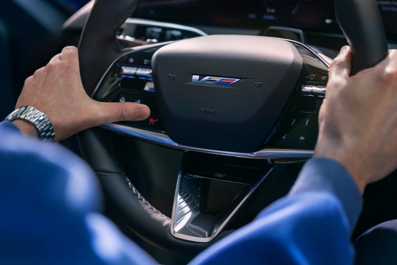 Close-up of a Man About to Press the V-Button on the 2026 OPTIQ-V Steering Wheel | Stevens Creek Cadillac in Santa Clara CA